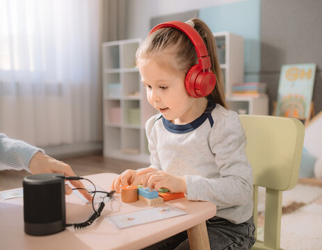 A child with red headphones listens to sound, focusing on auditory input for learning and sensory development. Early education for kids with developmental differences, exploring noise and sound.