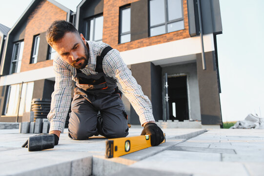Construction worker laying paving stones using level tool