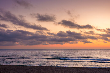 Obraz premium sunrise over the sea. beach landscape in golden glow. morning sky with purple clouds above horizon. scenery with calm waves. tranquil seascape wallpaper for summer vacation