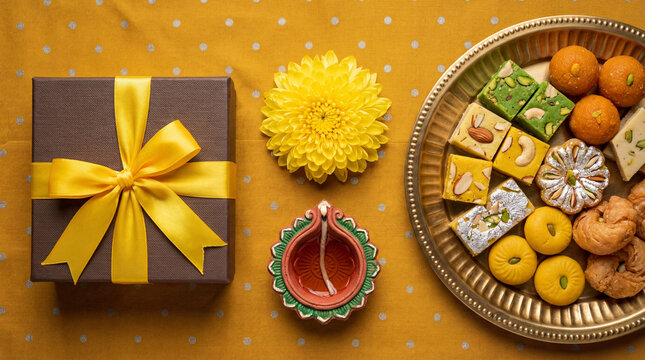 Diwali festival celebration with gift box, diya lamp, marigold flower and traditional indian sweets on a yellow background