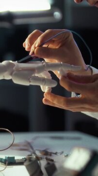 In high-tech workshop bathed in evening light, an engineer carefully solder-connects wires to a robotic hand prototype, fine-tuning its circuitry as precision and innovation drive the nocturnal build