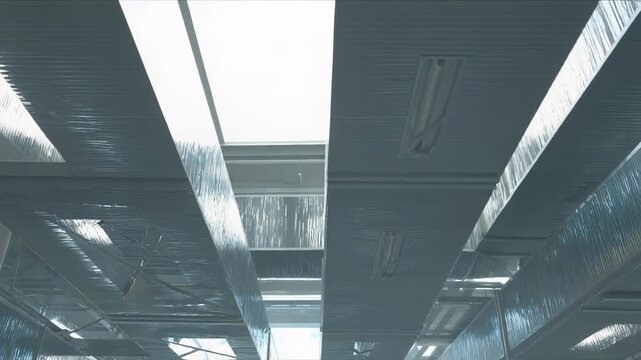 Industrial air ducts creating a complex ceiling structure, reflecting a bright light entering through windows, symbolizing modern construction and infrastructure technology