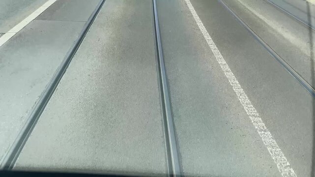 Tram intersection crossing viewed from cab window, mixed ballast and paved sections with turnout hardware, bus lane markings. Urban public transportation