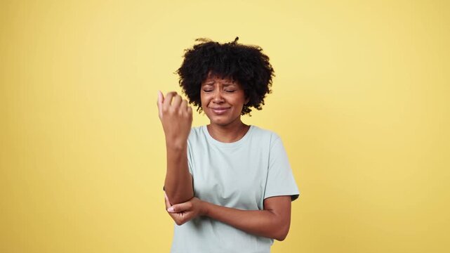 Young woman suffering from elbow pain on yellow background
