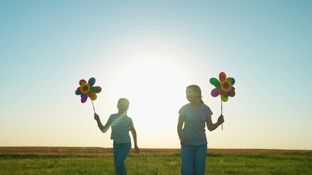 Happy children girls playing with toy pinwheel outside in summer park. Friends running with toy pinwheel in hand across green lawn. Child, childhood. Family picnic, nature. Teenage girl, nature, kids