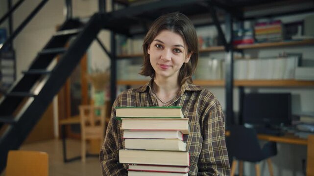 Student carries stack of books in library while preparing for study session during the day