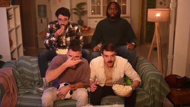 Four male friends watching football match on tv and celebrating victory with excitement and joy at home
