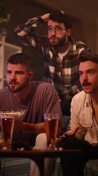 Disappointed male friends watching a tense sports game on television at home getting upset