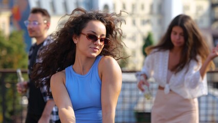 Obraz premium Close up of young brunette woman having fun with friends at sunset disco moving rhythmically to music. Pretty woman dancing at party outdoor on rooftop. Summer partying