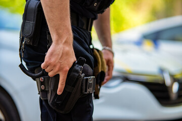 A close-up, side-profile shot of a police officer or tactical unit member standing in front of a blurred white patrol car © TetianaRUD