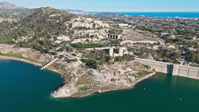 Drone descending from a high altitude to a one meter level over a calm Amadorio reservoir revealing the scale of the dam wall and its mirror reflection
