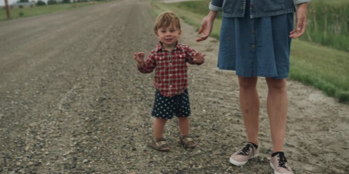 Toddler holding hands with a parent on a gravel path