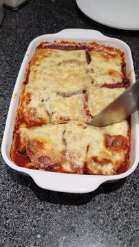 A person cutting a homemade freshly baked eggplant parmigiana, the tomato sauce expands with the pression over the cheese crust.  
