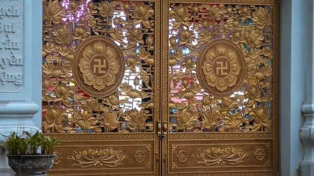 Massive majestic golden gates of Viet Nam Quoc Tu Pagoda (Vietnamese National Pagoda) carved with floral patterns and adorned with holy swastikas. Ho Chi Minh City, Vietnam