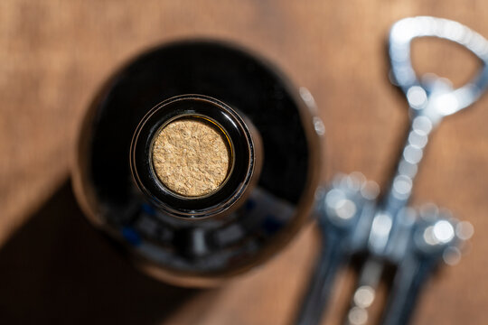 Closeup top view of dark glass wine bottle sealed with natural cork next to a metal corkscrew on a wooden background. Perfect for wine tasting and restaurant themes. Wine bottle with cork and opener