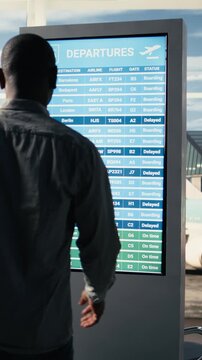 Vertical Video Diverse passengers panicking inside international airport terminal after all flights cancelled, shown in red on departures information board. Travelers appear angry by disrupted travel