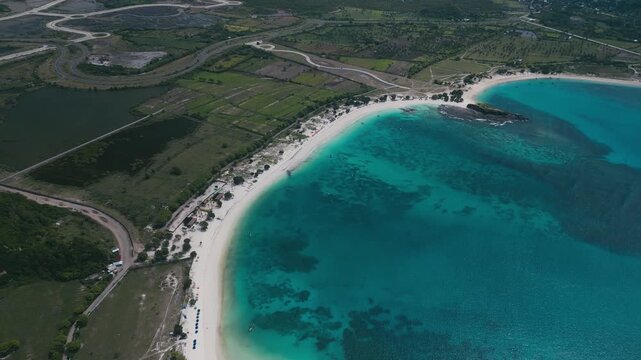 Aerial View Emerald Lagoon With Curved White Beach, Adjacent Farmland And Green Hills, Clear Shallow Patches And Reef Patterns, Calm Atmosphere Suited For Nature And Travel Visuals,Lombok
