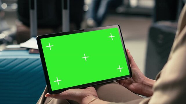 Green screen tablet in busy airport waiting area with travelers near gate, holding boarding pass and ticket as they prepare to board airplane for international flight. Air travel for holiday.