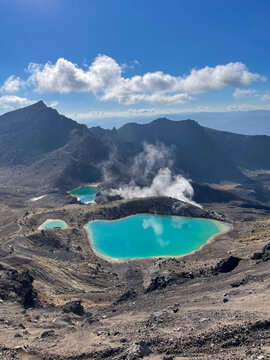 Stunning high-angle view of the vibrant Emerald Lakes and steam vents in Tongariro National Park, New Zealand. Dramatic volcanic crater landscape along the Tongariro Alpine Crossing hike, blue sky.