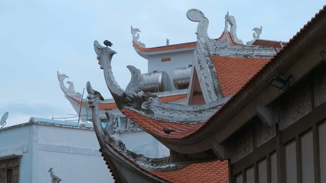 A pigeon is sitting on the head of a phoenix style chofah decorating the edge of multi-tiered roofs of the Vinh Nghiem Pagoda in Ho Chi Minh City, Vietnam