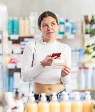 Young woman scans the barcode of a package with pills and medicines on her mobile phone, she reads the information on the pharmacy's website before buying