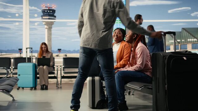 Family of travelers with teenage girl sitting together in airport terminal waiting area, smiling and talking while holding plane tickets and passports. Vacation air travel to a holiday destination.