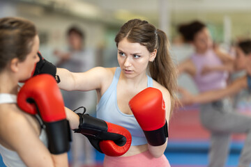 Obraz premium Women in boxing gloves practice boxing punches in pairs in gym