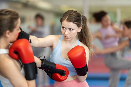 Women in boxing gloves practice boxing punches in pairs in gym