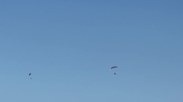 Two paragliders in a clear blue sky,Skydiver under a red parachute in a bright clear sky, low angle view of paragliding extreme sport, minimalistic aerial freedom concept.
