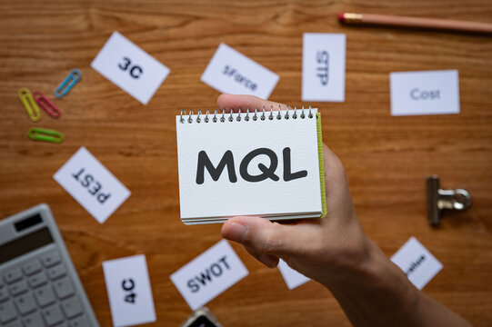 Eye-catching image of MQL text on notebook. The word stands for Marketing Qualified Lead. Shown with calculator, clips, pen.