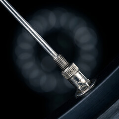 Extreme close-up of a bicycle valve stem on a rim, with soft circular bokeh background emphasizing precision, inflation, and clean mechanical detail.