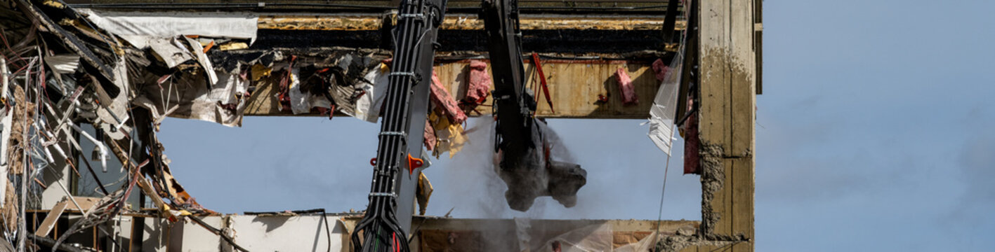 Urban redevelopment, hydraulic jaw of cracker attachment tearing down and demolishing an old concrete office building, heavy duty construction equipment at work on project
