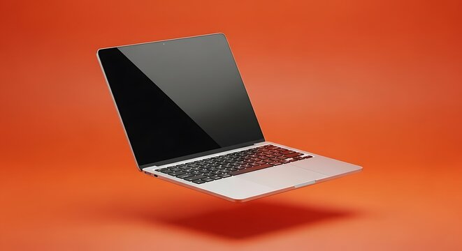 Silver laptop computer floating in mid air over a vibrant orange studio background with a blank black screen for digital mockup and technology