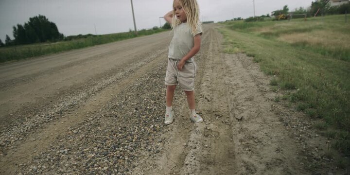 Young boy standing alone on a dirt road in the countryside throwing rocks