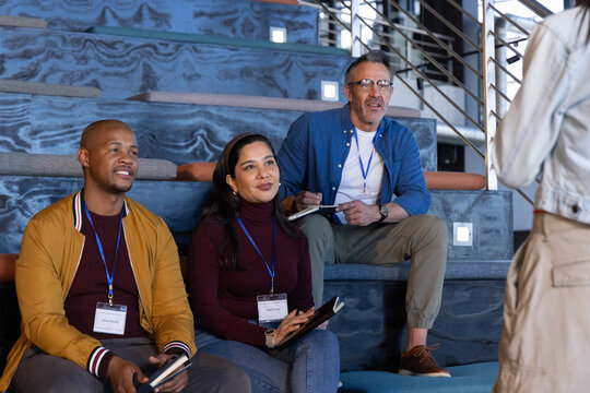 Diverse attendees sitting on tiered blue-marble steps listening and taking notes with lanyards