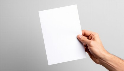 Obraz premium Hand holding blank white paper mockup against neutral gray background for design and advertising
