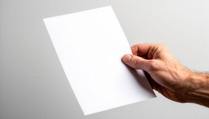 Obraz premium Hand holding blank white paper mockup against neutral gray background for branding and design presentation