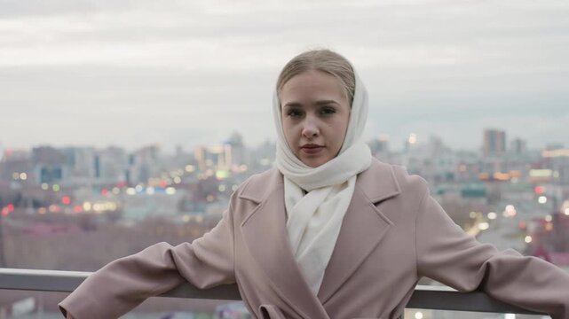 Caucasian woman arms out against city skyline at twilight coat and scarf fluttering confident model posing for evening editorial, panoramic lights and calm horizon amplify empowerment tone