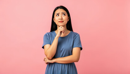 Fototapeta premium Contemplative Woman's Pondering: An Asian woman, captured in a studio setting, is deep in thought, her expression hinting at a complex issue or challenging decision.