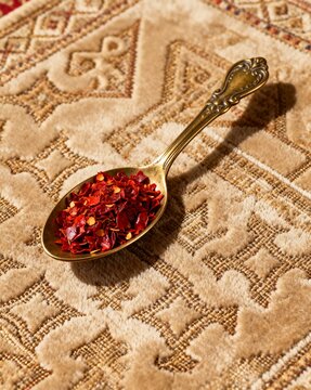 Dried Aleppo Pepper Flakes on Ornate Spoon over Textured Fabric