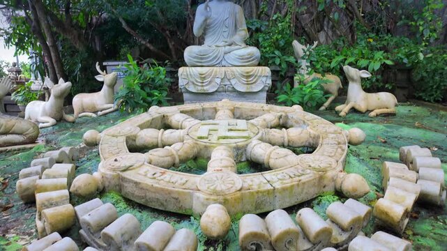 A serene Buddha statue sits among deer sculptures and a Dharma wheel in the gardens of The Marble Mountains, in DA NANG, Vietnam. The statues symbolize peace and harmony.