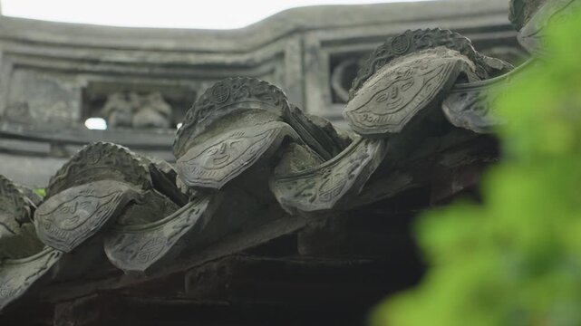 Closeup traditional roof tiles weathered eaves, soft green foliage bokeh, aged ceramic curves with subtle moss texture, ornate ridge relief, overcast light and calm garden atmosphere evoking historic