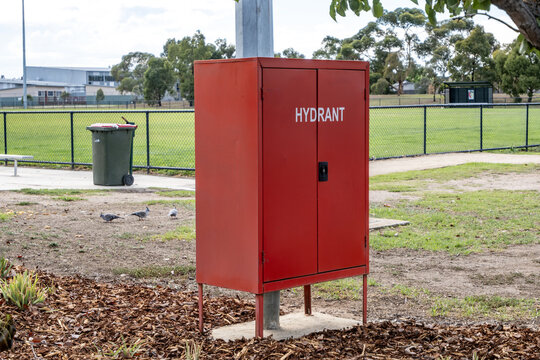Red fire hydrant cabinet in a public park in Australia, near open spots field. Essential emergency infrastructure supporting fire protection, safety systems, and municipal services in public space