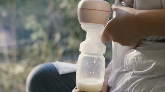 Woman holding breast pump outdoors sitting.
