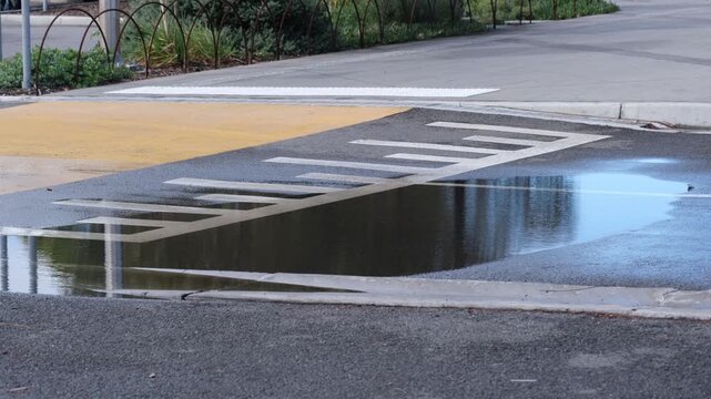 Water pooling on a suburban street intersection in Australia, forming a puddle over road markings and pedestrian crossing. Urban drainage issue highlighting stormwater management, surface design