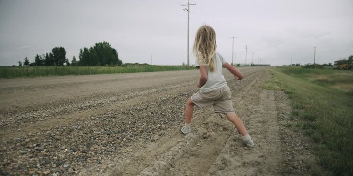 Young boy walking down a windy dirt road in the countryside and throwing rocks