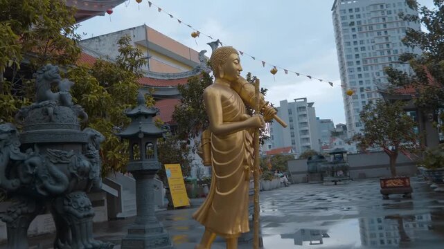 A golden statue of the Buddha holding a walking staff and a parasol stands in the temple garden of the famous Vinh Nghiem Pagoda in Ho Chi Minh City, Vietnam
