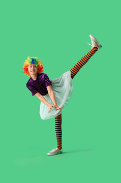 Funny girl in clown costume dancing on green background. April Fool's Day celebration