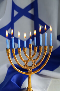 Hanukkah menorah with lit blue candles in front of Israeli flag, Jewish holiday celebration symbol, traditional candelabrum with star of David and festive religious background