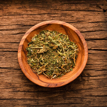 Close-up of dried and crushed Dysphania ambrosioides leaves in a handcrafted wooden bowl, highlighting their rustic and organic texture